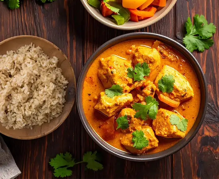 Bowl of chicken curry with brown rice on a wooden table