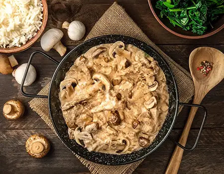 Beef Stroganoff in a black pan with mushrooms and greens on a wooden table