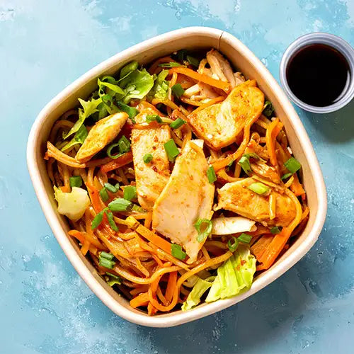 Bowl of salad with chicken and noodles with vegetables on a blue background