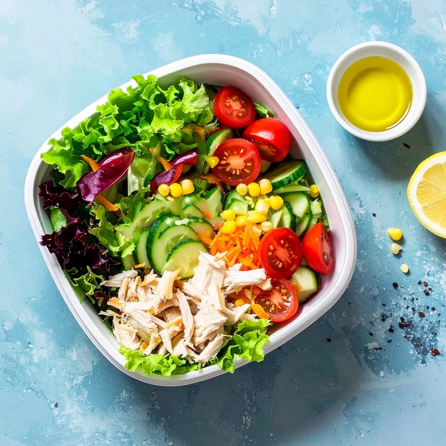 Colorful salad with chicken, vegetables, and a small bowl of dressing on a blue background
