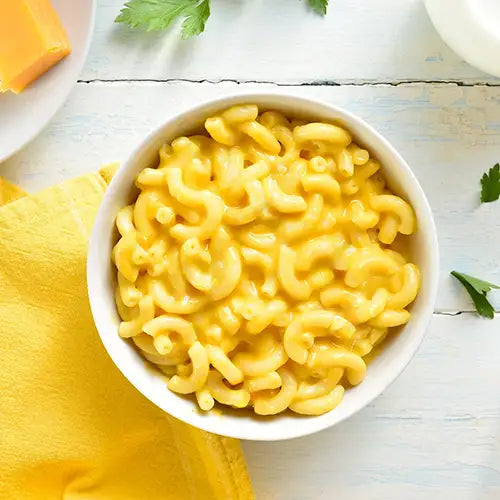 White bowl of macaroni and cheese on a white surface with a yellow napkin.
