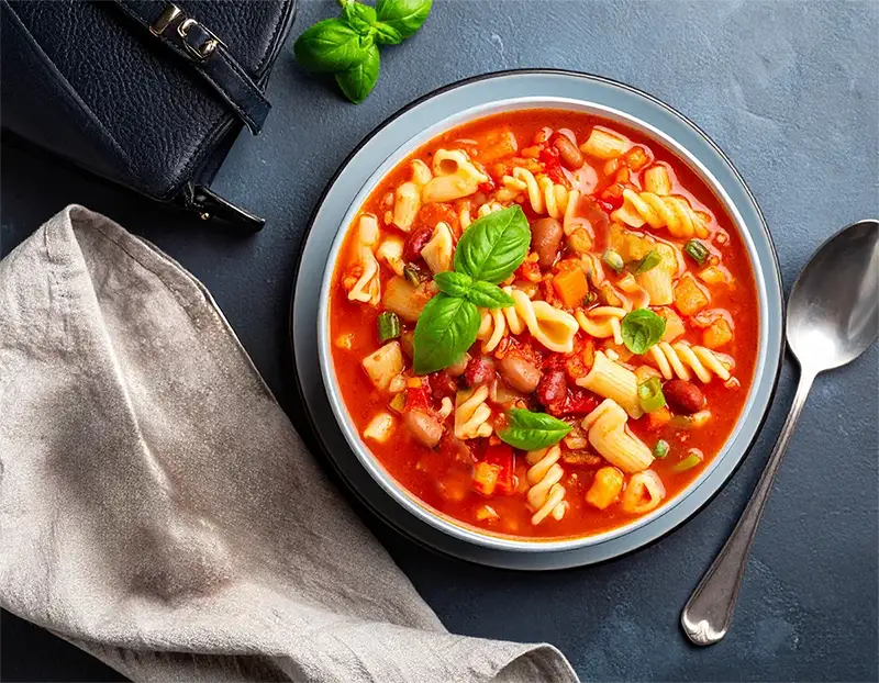 Bowl of minestrone soup with a spoon on a gray surface