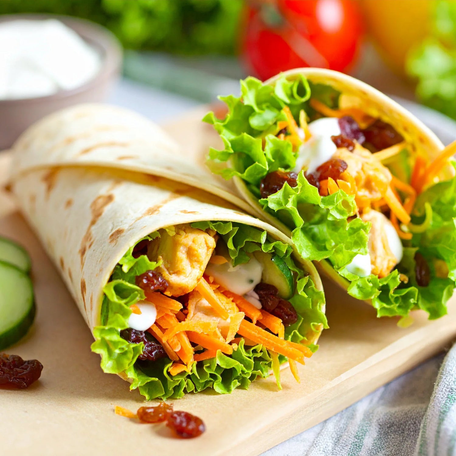 Moroccan Chicken wrap with lettuce, carrots, and raisins on a wooden board with a blurred background of vegetables.