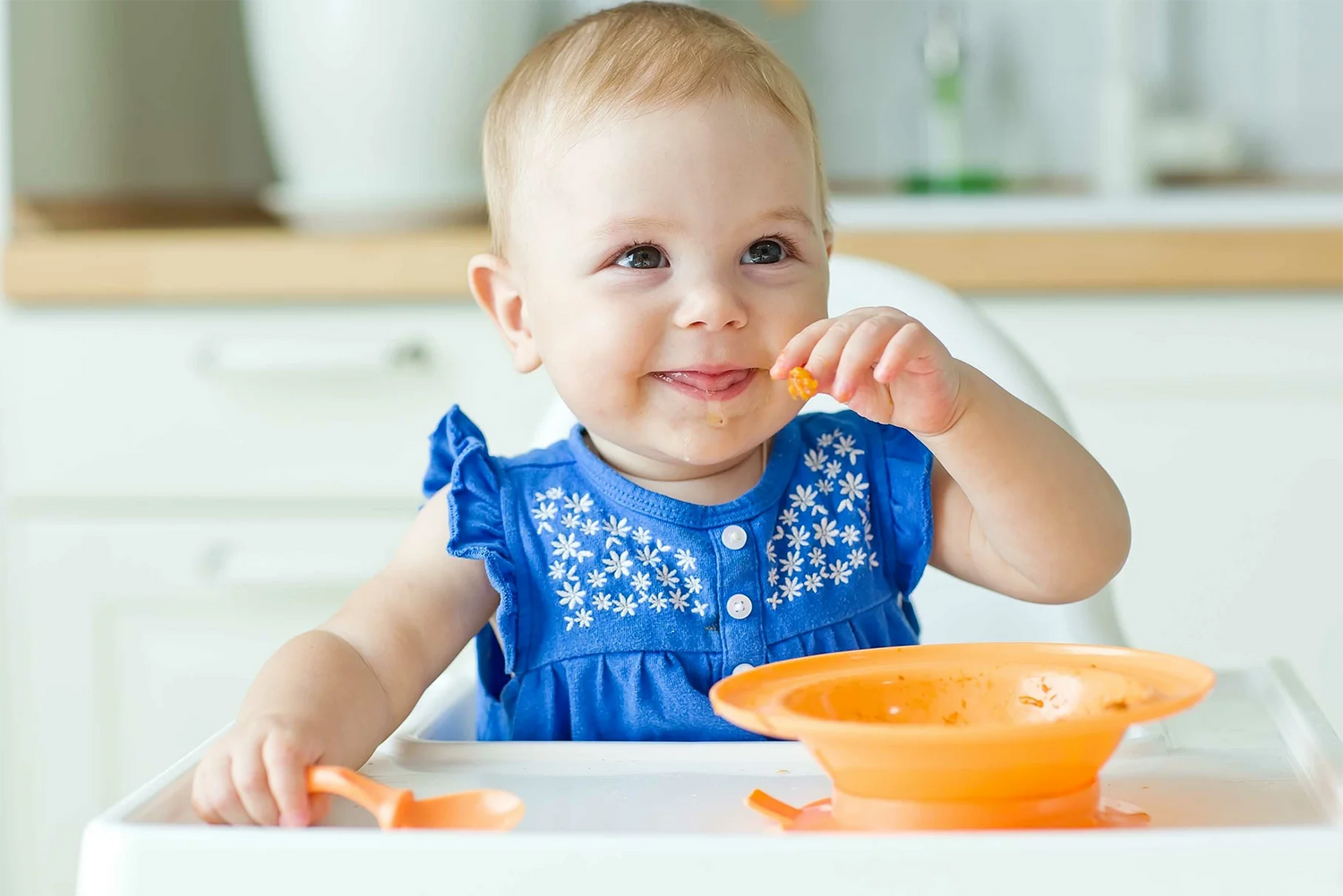Baby in high chair with orange bowl and spoon.