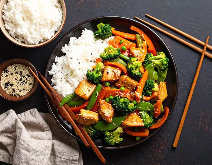 Plated dish of Teritaki stir-fry of chicken and vegetables with rice, accompanied by chopsticks on a dark surface.