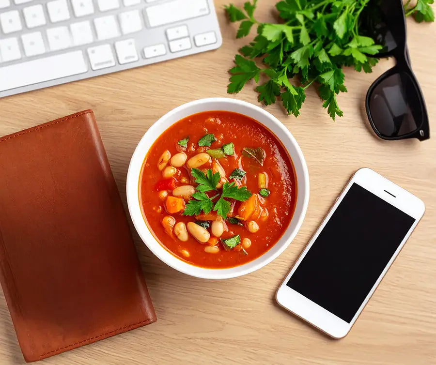 Bowl of Tuscan Vegetable Soup on a desk with phone, wallet, and keyboard