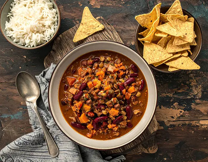 Bowl of chili with tortilla chips and rice on a wooden table