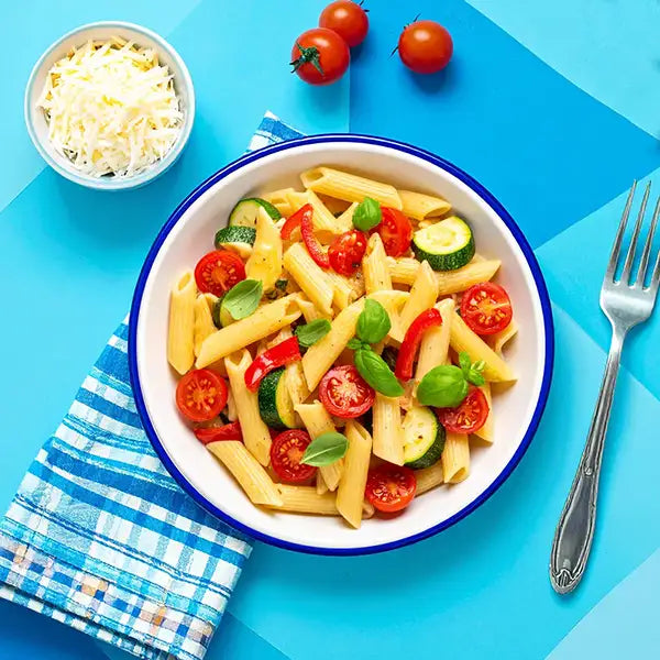 Pasta salad with tomatoes and zucchini in a white bowl on a blue background