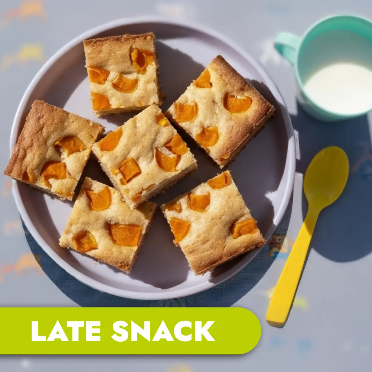 TLG Childcare catering late snack. Square slices of cake with apricot pieces on a plate with a yellow spoon and green cup.